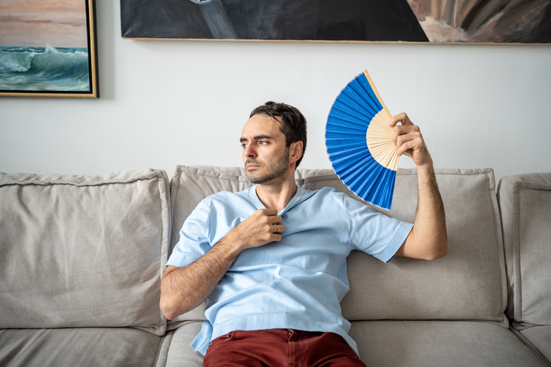 Hombre en sofá abanicándose por el calor